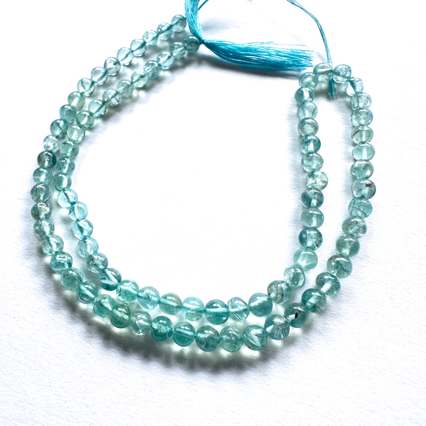 Close-up of Apatite beads showcasing their glossy surface and vibrant oceanic colour.