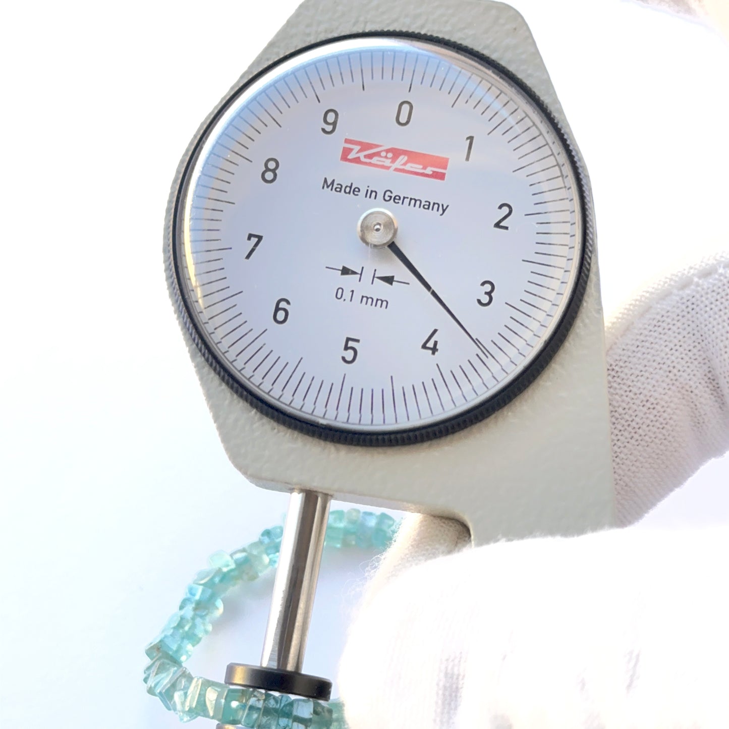 A dial gauge measures the Apatite smooth square Heishi 3.5–4mm gemstone.