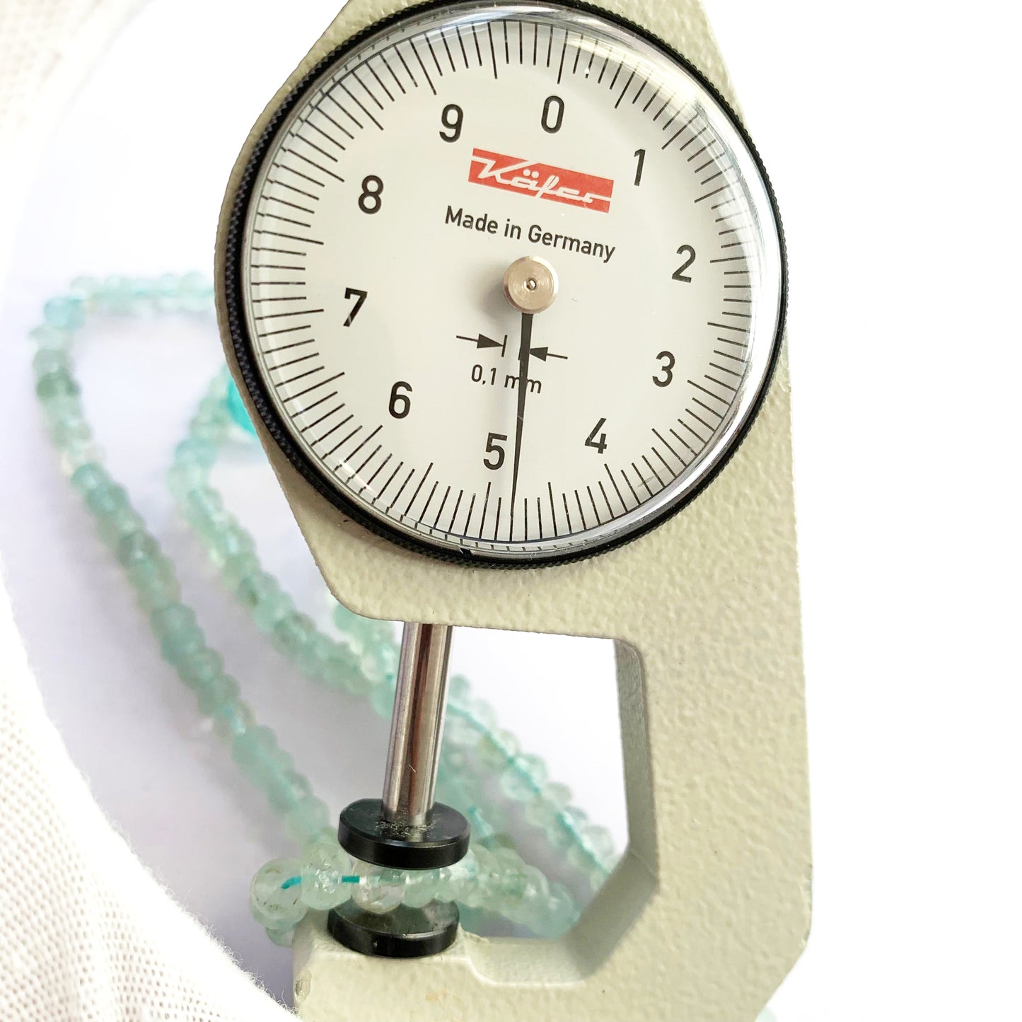 A dial gauge measures the Aquamarine faceted rondelle 4.5-5mm gemstone.