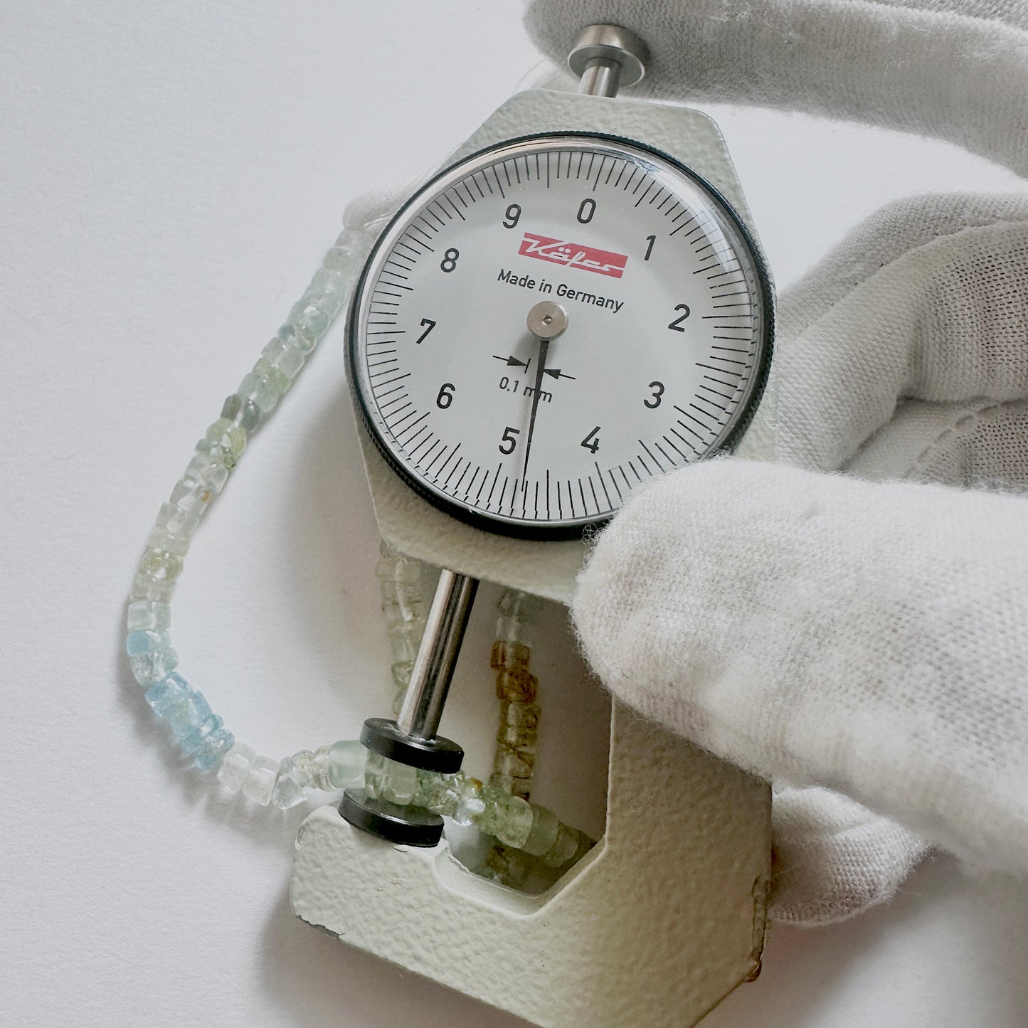 A dial gauge measures the Aquamarine Smooth Wheel 4.5-4.8mm gemstone.