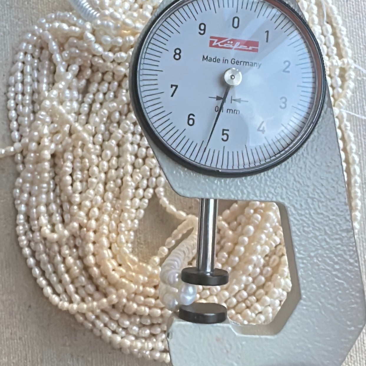 A dial gauge measures the Baroque Rice Pearls rice cut 4.2 x 5.4mm gemstone for accuracy.