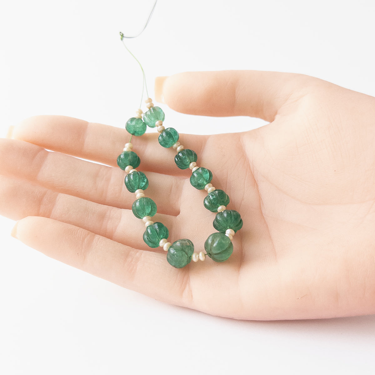A person holds delicate pieces of Beryl and Shell Pearl beads, showcasing their pumpkin cut design.