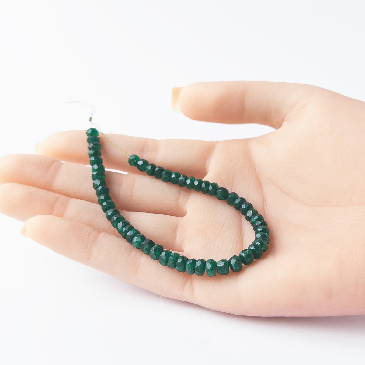 A person holds delicate pieces of Beryl beads, showcasing their faceted rondelle design.