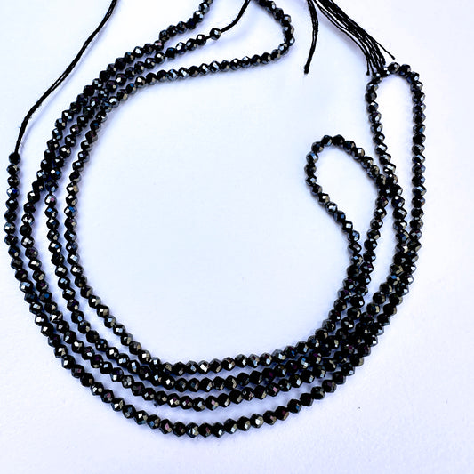 Close-up of coated Black Spinel stone beads showing faceted cut and enhanced shine.