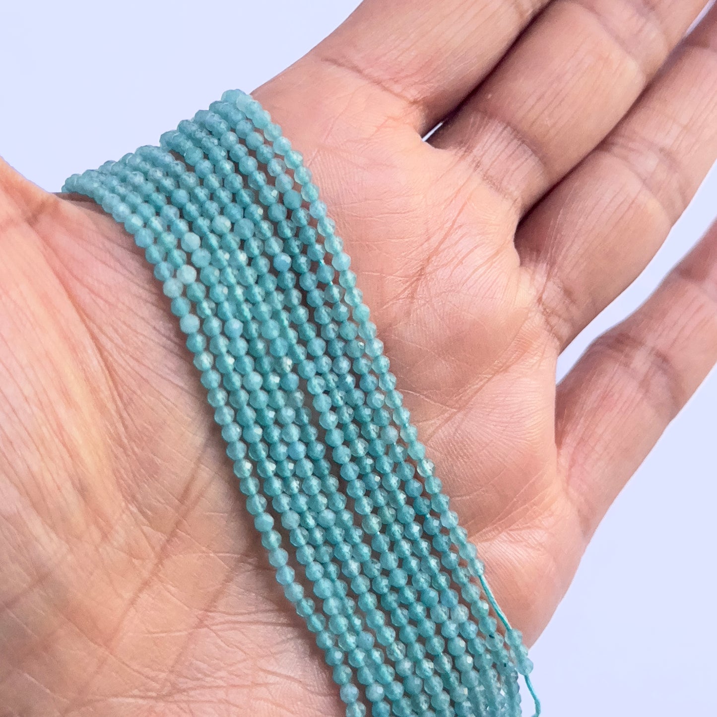 A person holds delicate strands of Chalcedony beads, showcasing their smooth design.
