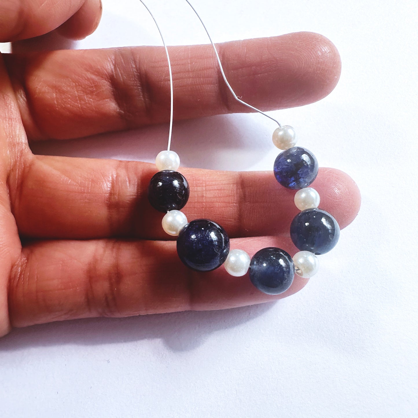 A person holds delicate strands of Blue Sapphire beads, showcasing their smooth design.