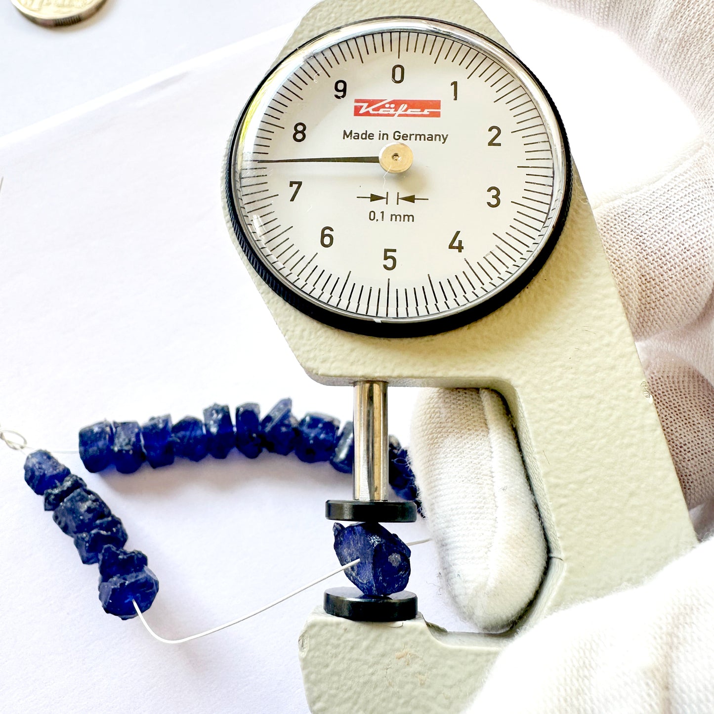 A dial gauge measures the Blue Sapphire rough 6-8mm gemstone bead.