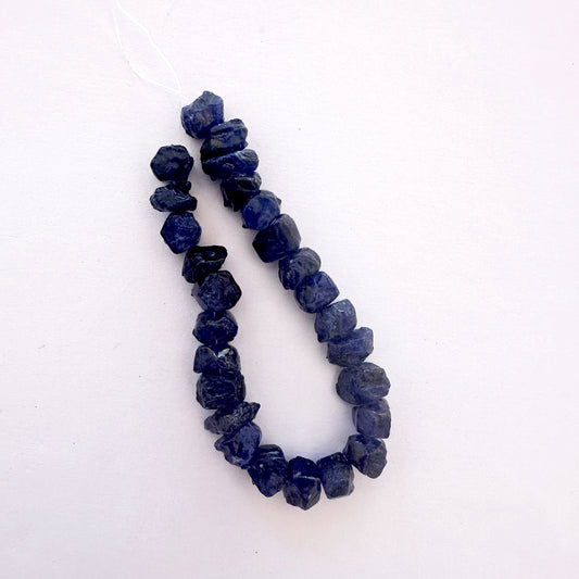 Close-up of raw blue sapphire gemstones arranged in a 34-piece strand with natural texture.