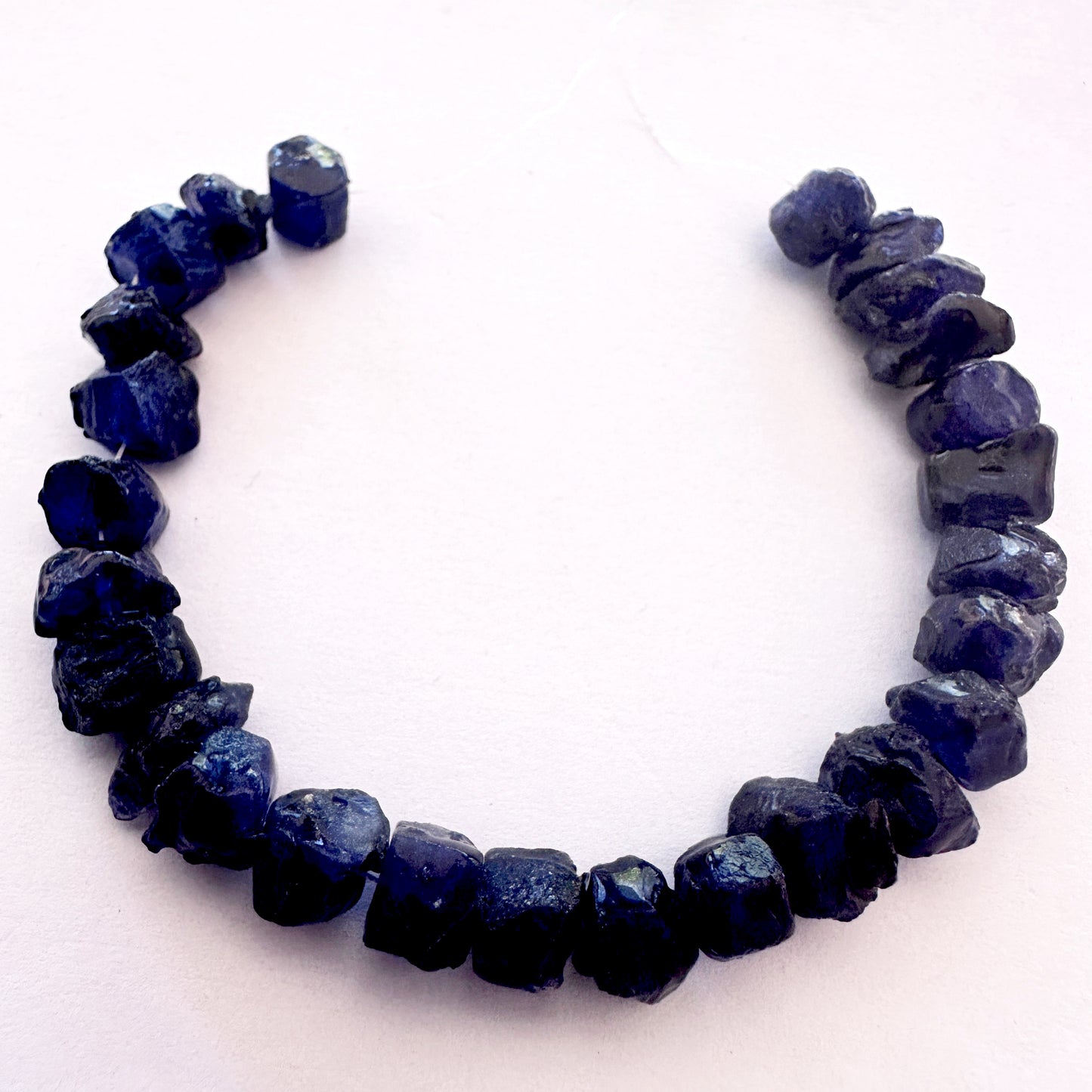 Faceted light reflecting off rough blue sapphire beads with rich navy colour.