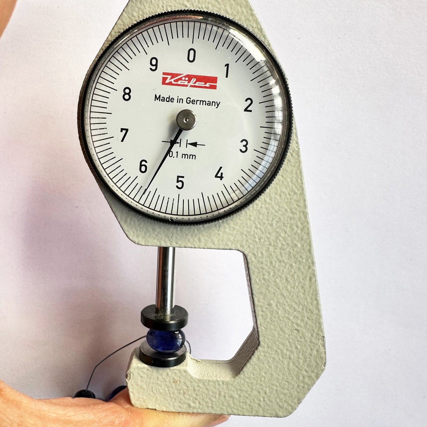 A dial gauge measures the Blue Sapphire smooth oval 7x5.5mm gemstone, ensuring precise sizing.