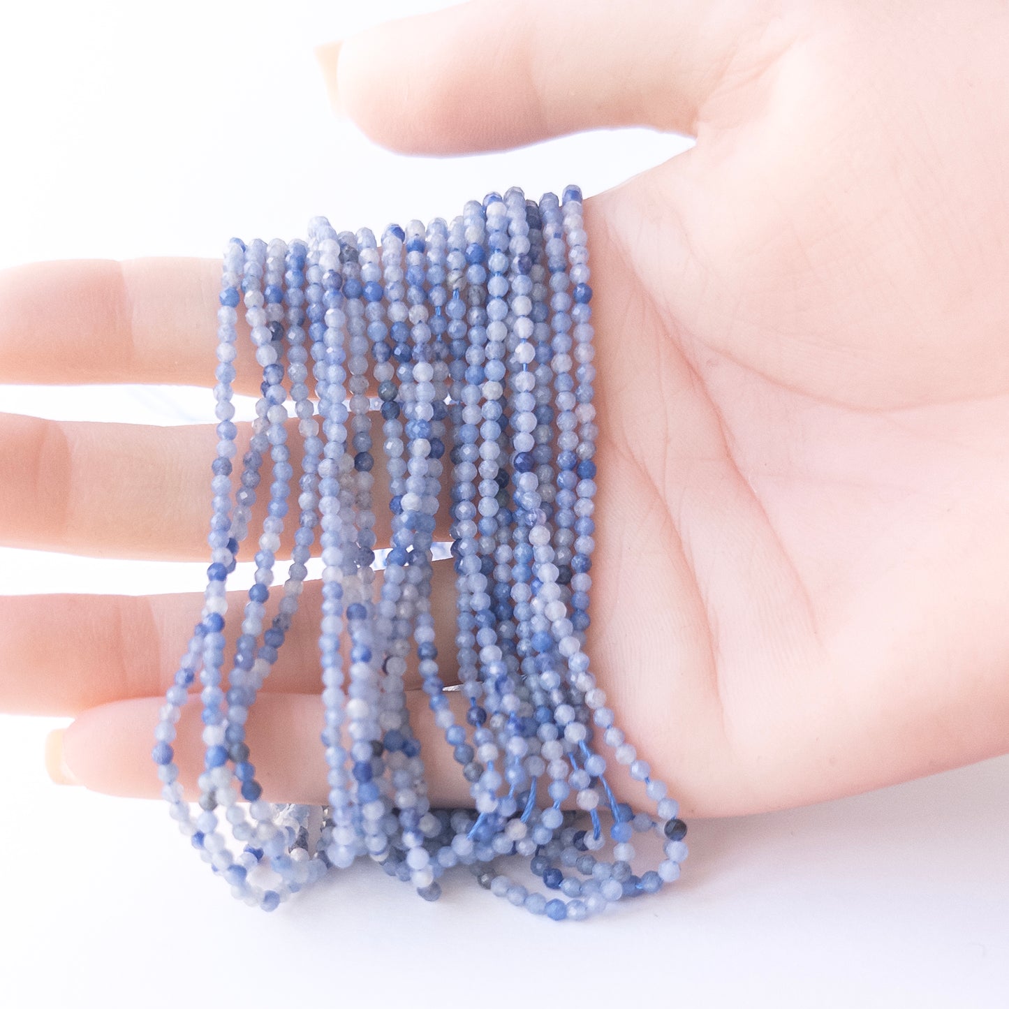 A person holds delicate strands of Blue Shaded Chalcedony beads, showcasing their faceted rondelle design.