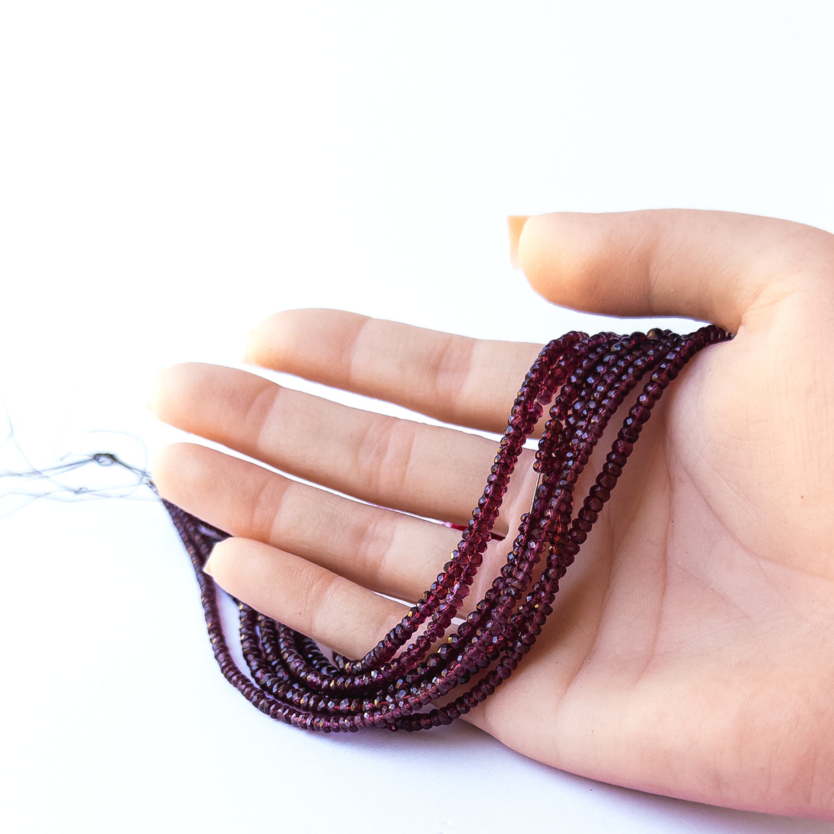 A person holds strands of Burma Garnet beads, showcasing their faceted rondelle design.