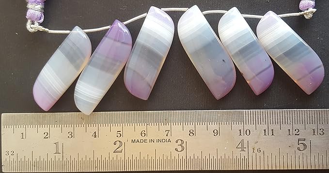 A close-up of a person measuring a purple Chalcedony,with a ruler.