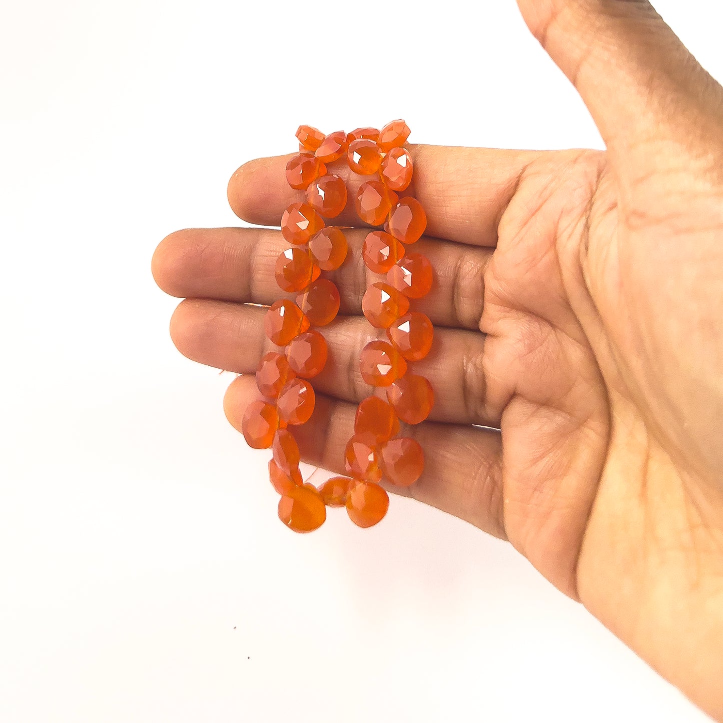 A person holds delicate strands of Carnelian beads, showcasing their faceted briolette design.