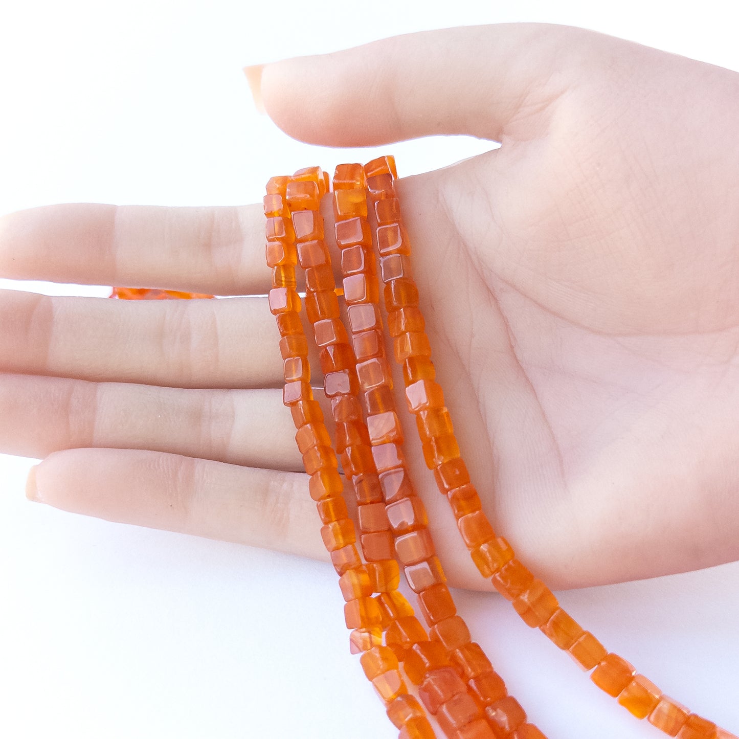 A person holds delicate strands of Carnelian beads, showcasing their smooth cube design.
