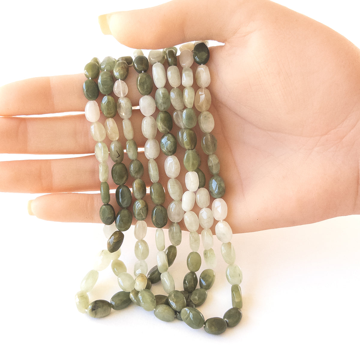 A person holds delicate strands of Cat’s Eye beads, showcasing their smooth oval design.