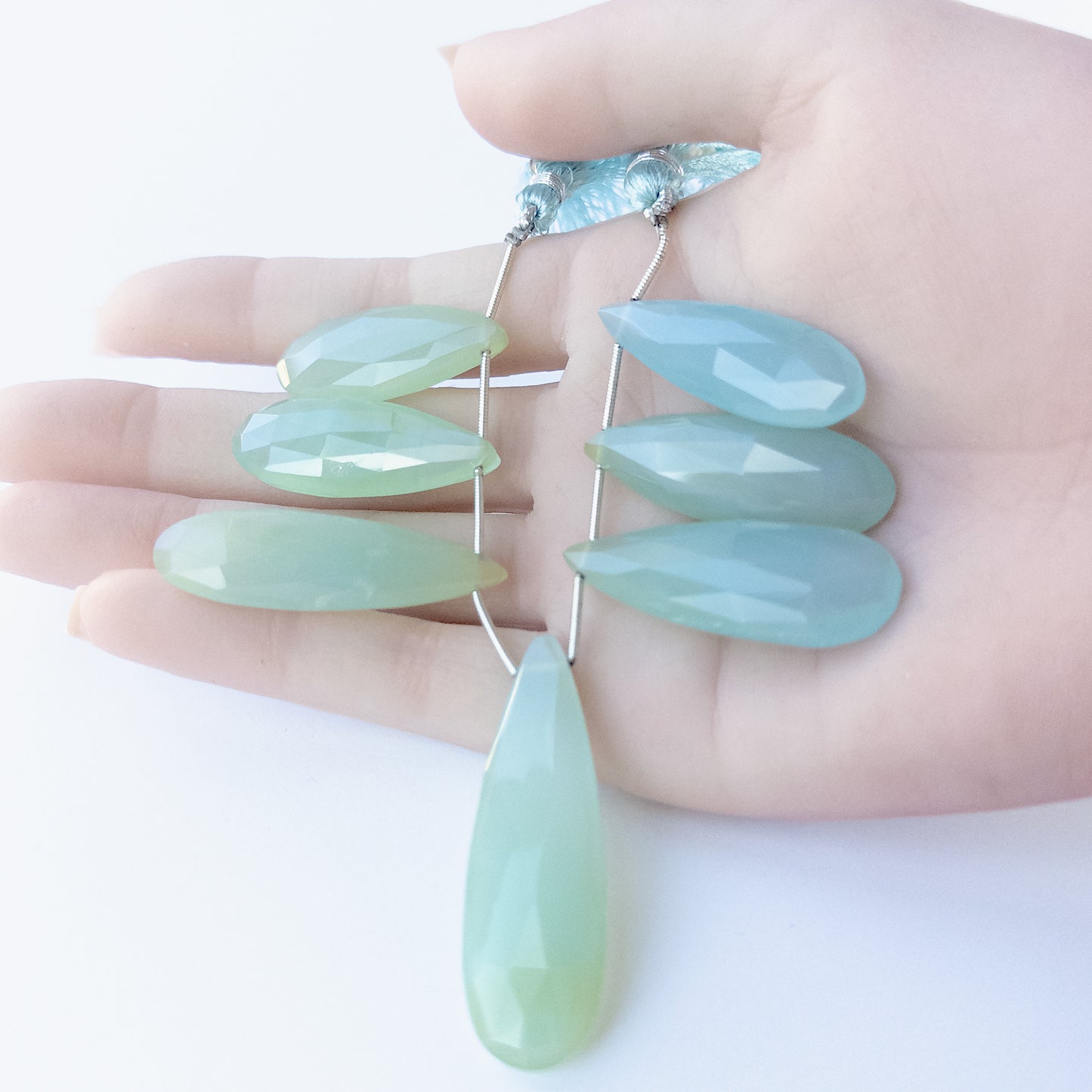 A person holds Chalcedony briolette pieces, showcasing their faceted teardrop design and size variation.