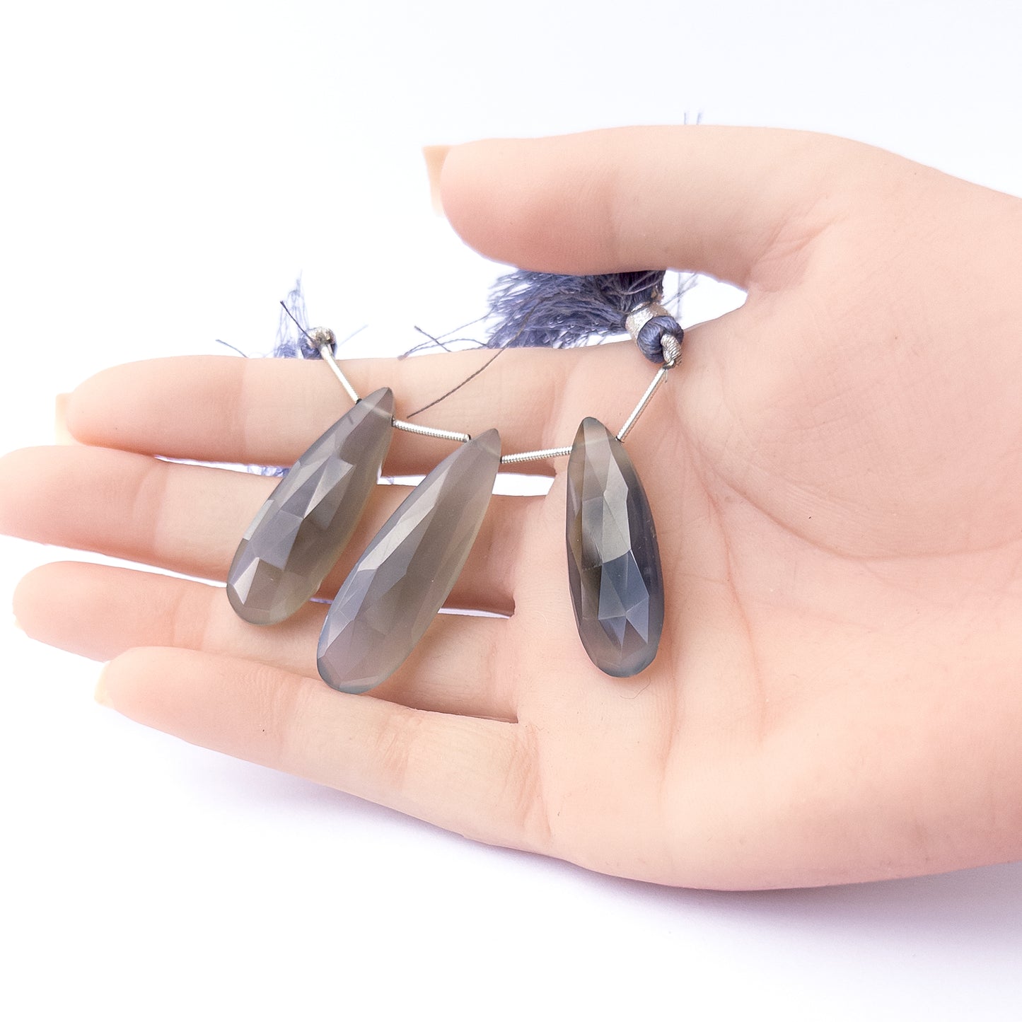 A person holds delicate strands of Chalcedony beads, showcasing their faceted briolette design.
