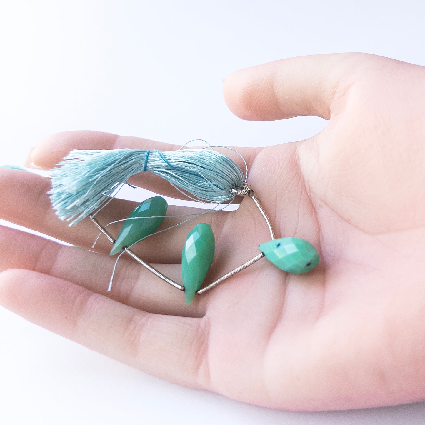 A person holds delicate pieces of Chalcedony beads, showcasing their faceted briolette design & imprefections.