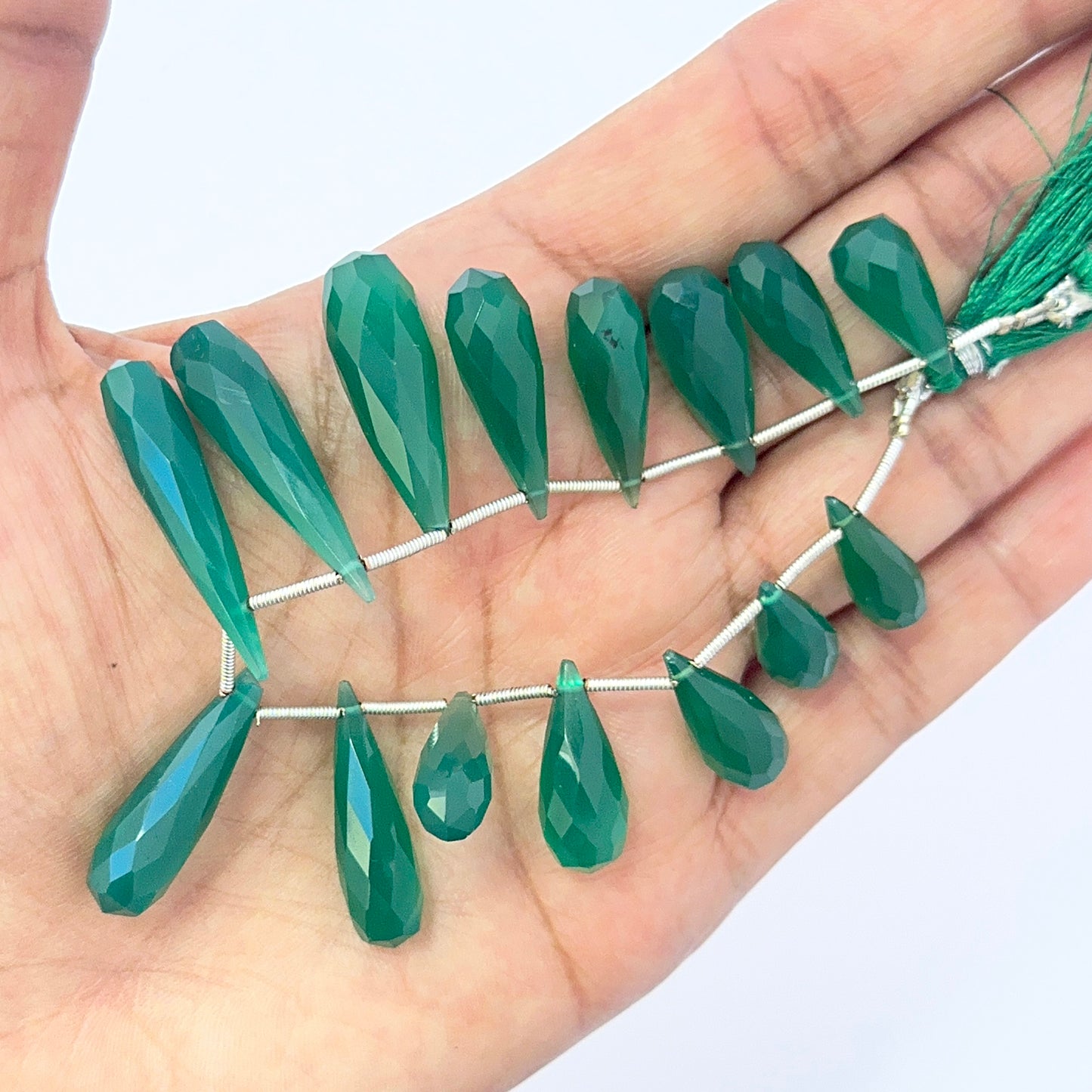 A person holds delicate strands of green Chalcedony beads, showcasing their smooth design.