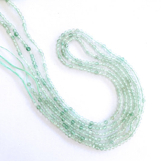 A person holds delicate strands of Chalcedony beads, showcasing their faceted design.