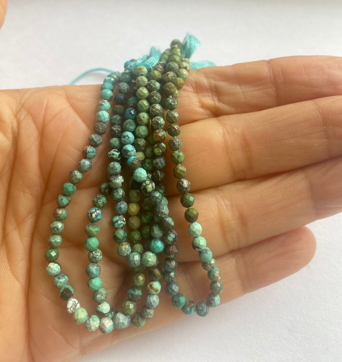 A person holds delicate strands of Chrysocolla beads, showcasing their faceted design.