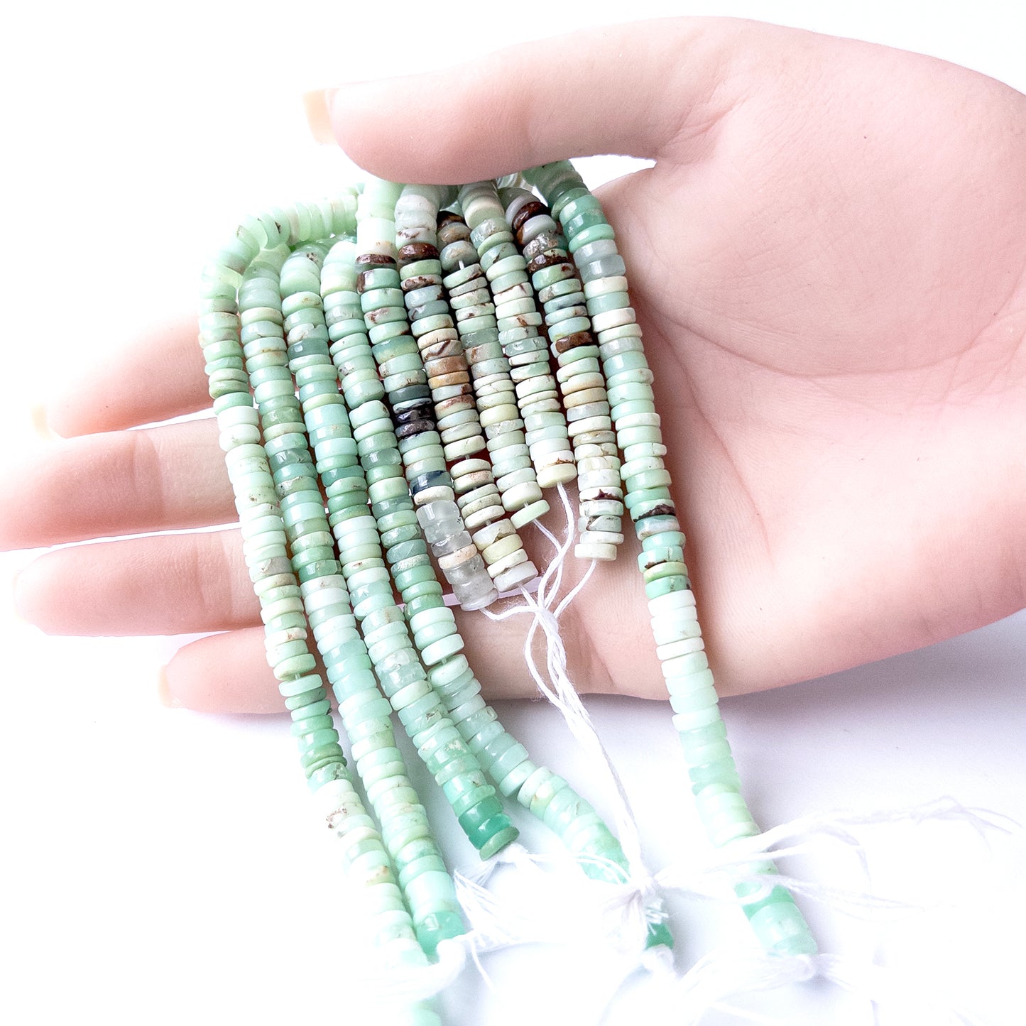 A person holds delicate strands of Chrysoprase beads, showcasing their smooth wheel heishi design.