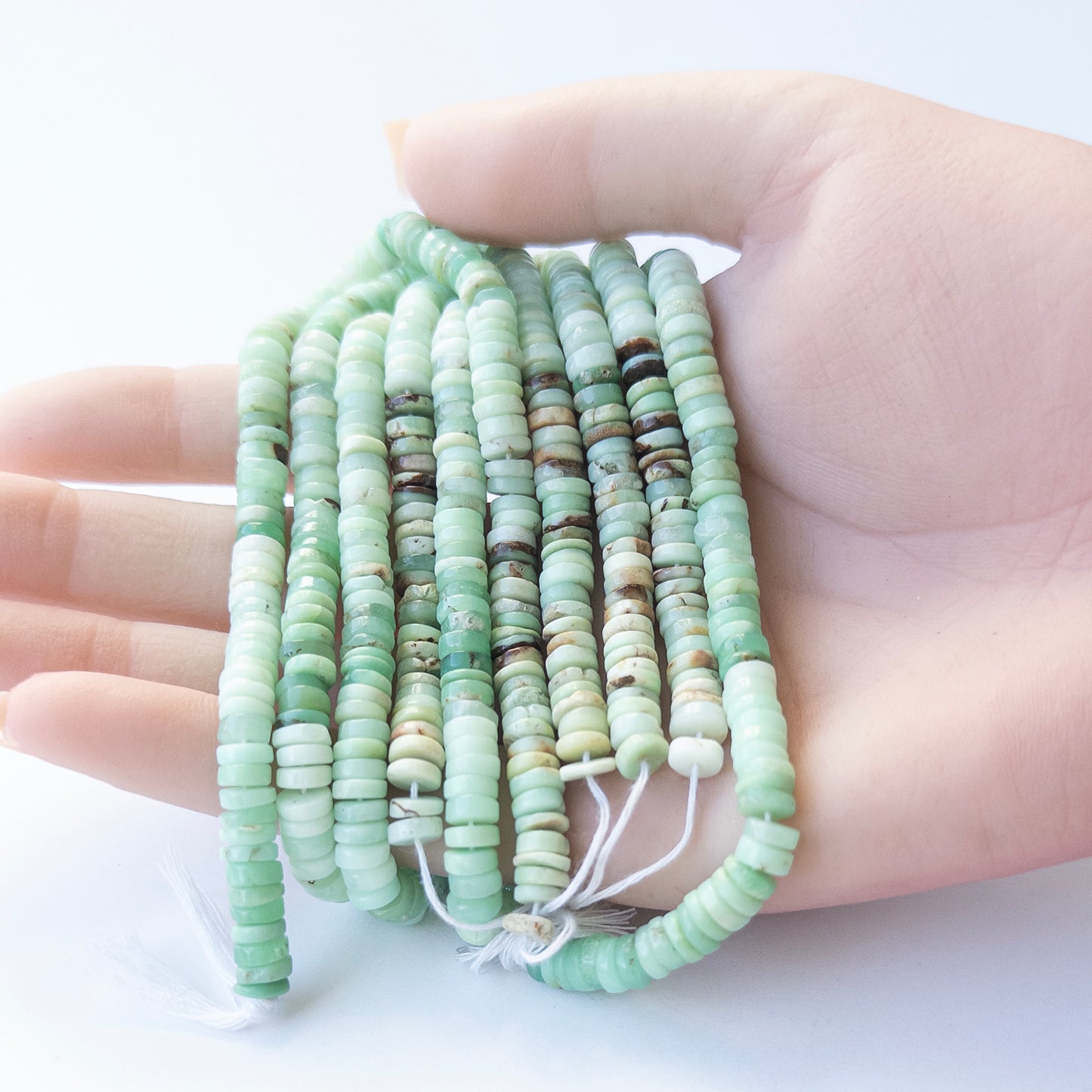 A person holds delicate strands of Chrysoprase beads, showcasing their smooth wheel design.