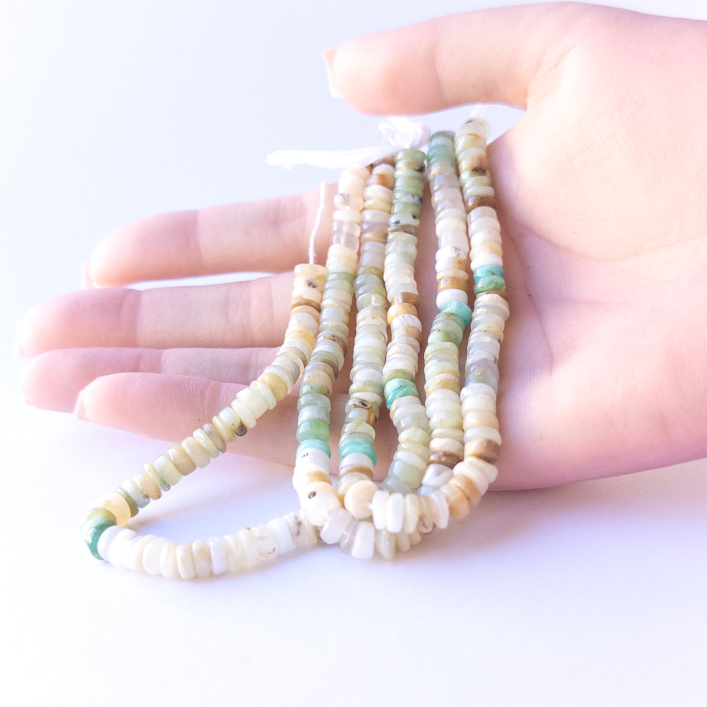 A person holds delicate strands of Chrysoprase beads, showcasing their Smooth Wheel design.