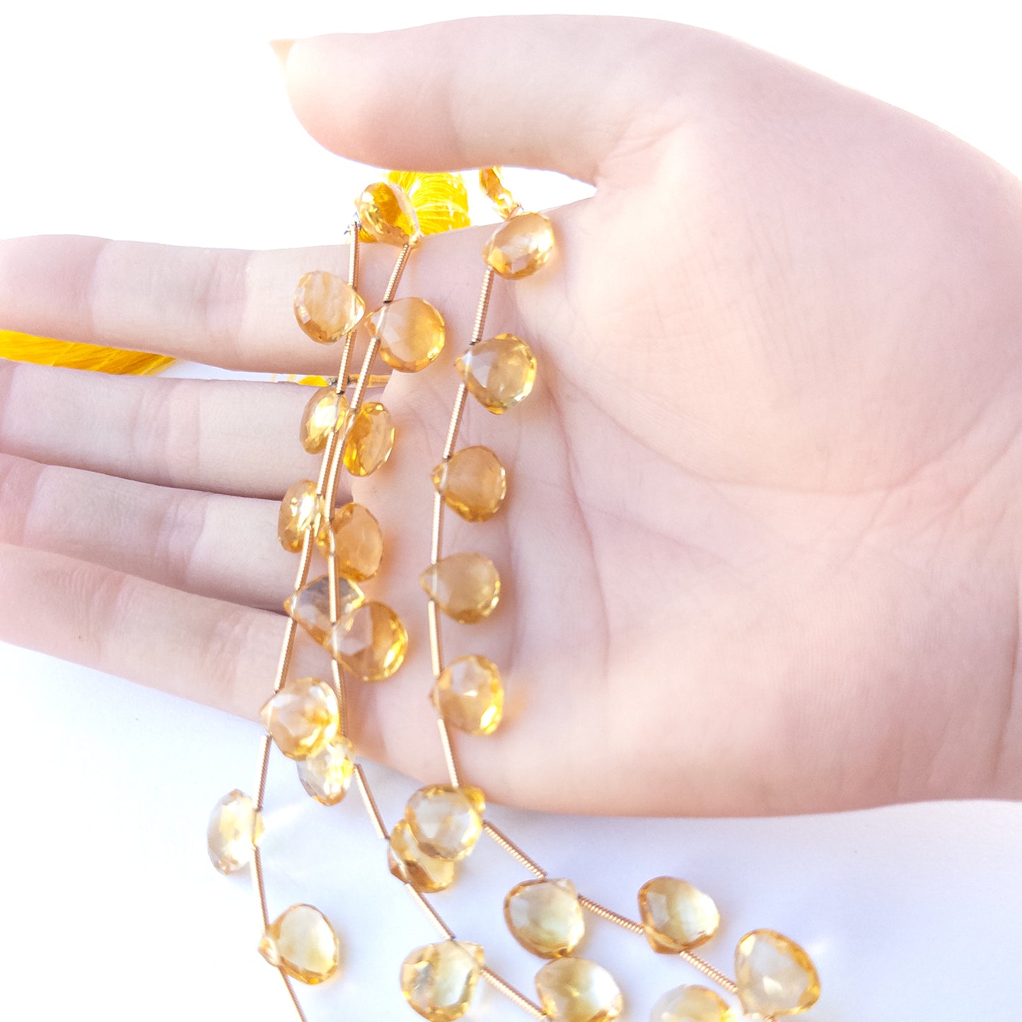 A person holds delicate strands of Citrine beads, showcasing their faceted briolette design.