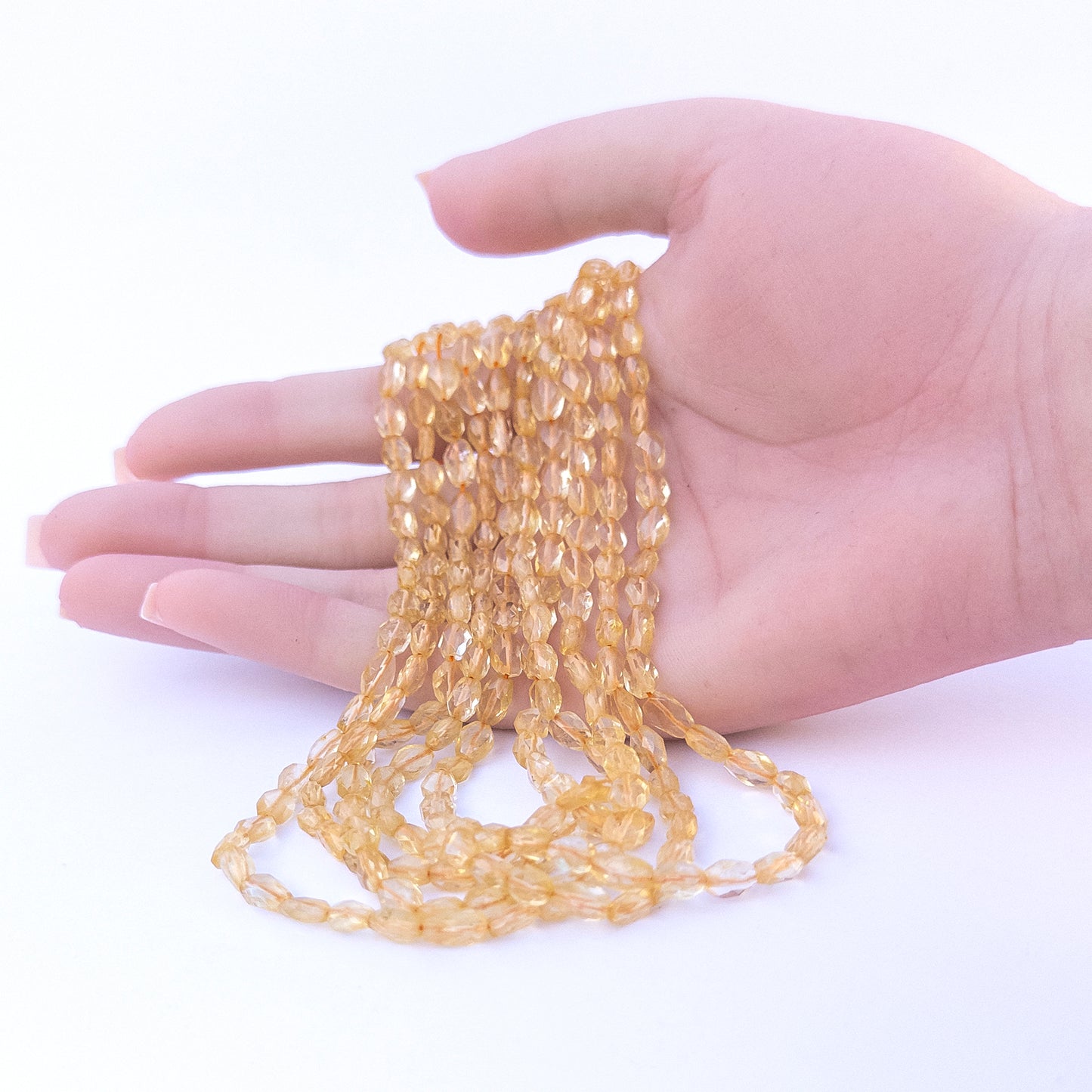 A person holds delicate strands of Citrine beads, showcasing their Faceted Oval design.