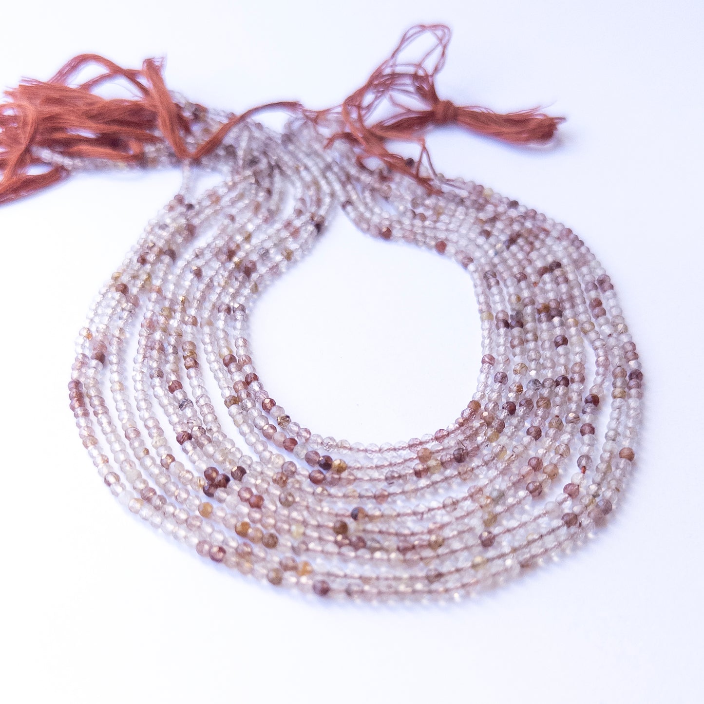A person holds delicate strands of Copper Rutile beads, showcasing their faceted rondelle design.