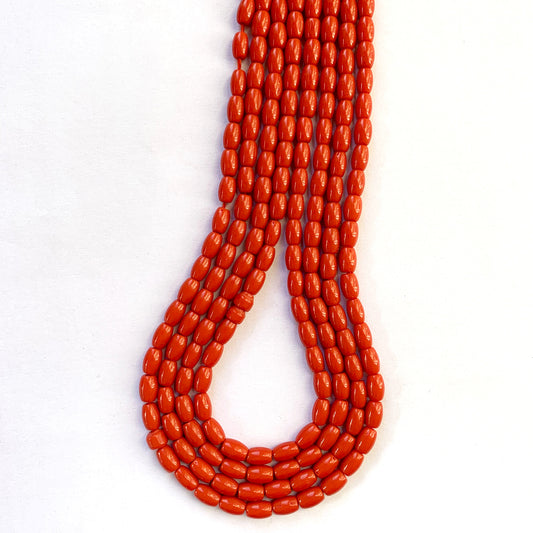 Vibrant coral beads with cylindrical cuts arranged evenly for handmade jewellery projects.