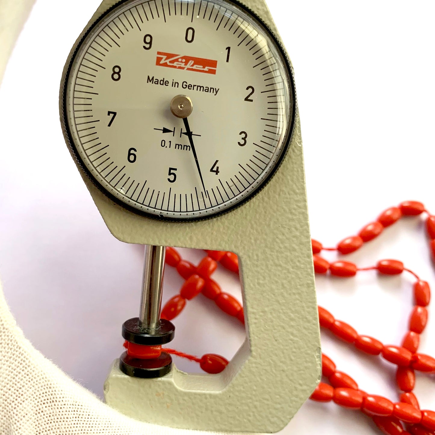 A dial gauge measures the Coral drum cut 6.7x4.4mm gemstone.