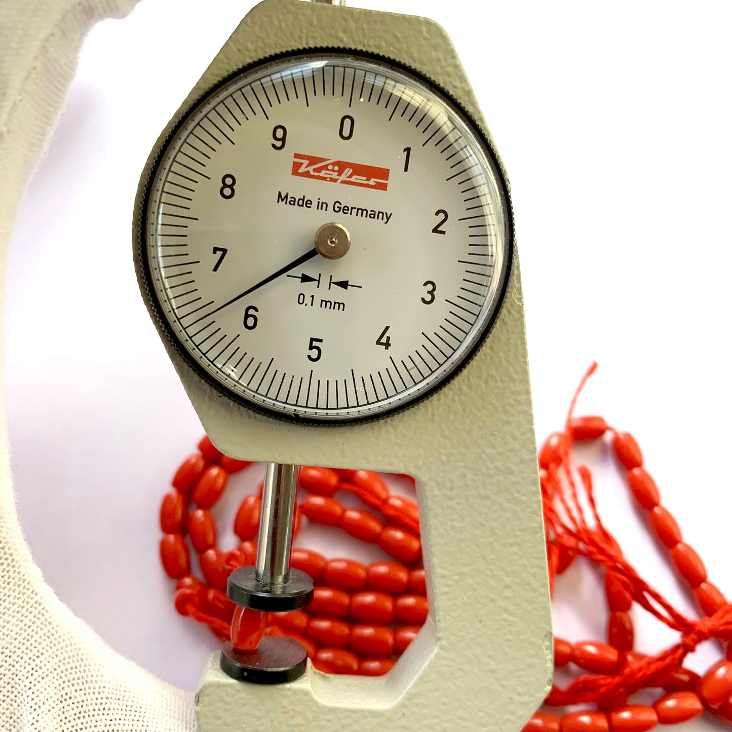A dial gauge measures the Coral drum cut 6.7x4.4mm gemstone.