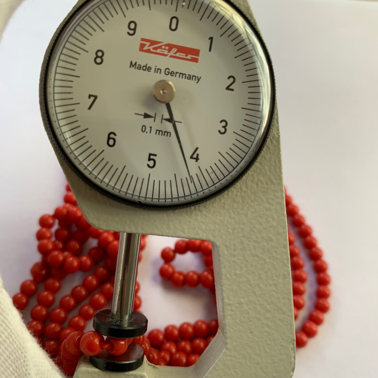 A dial gauge measures the Coral smooth round 4.3-4.5mm gemstone.