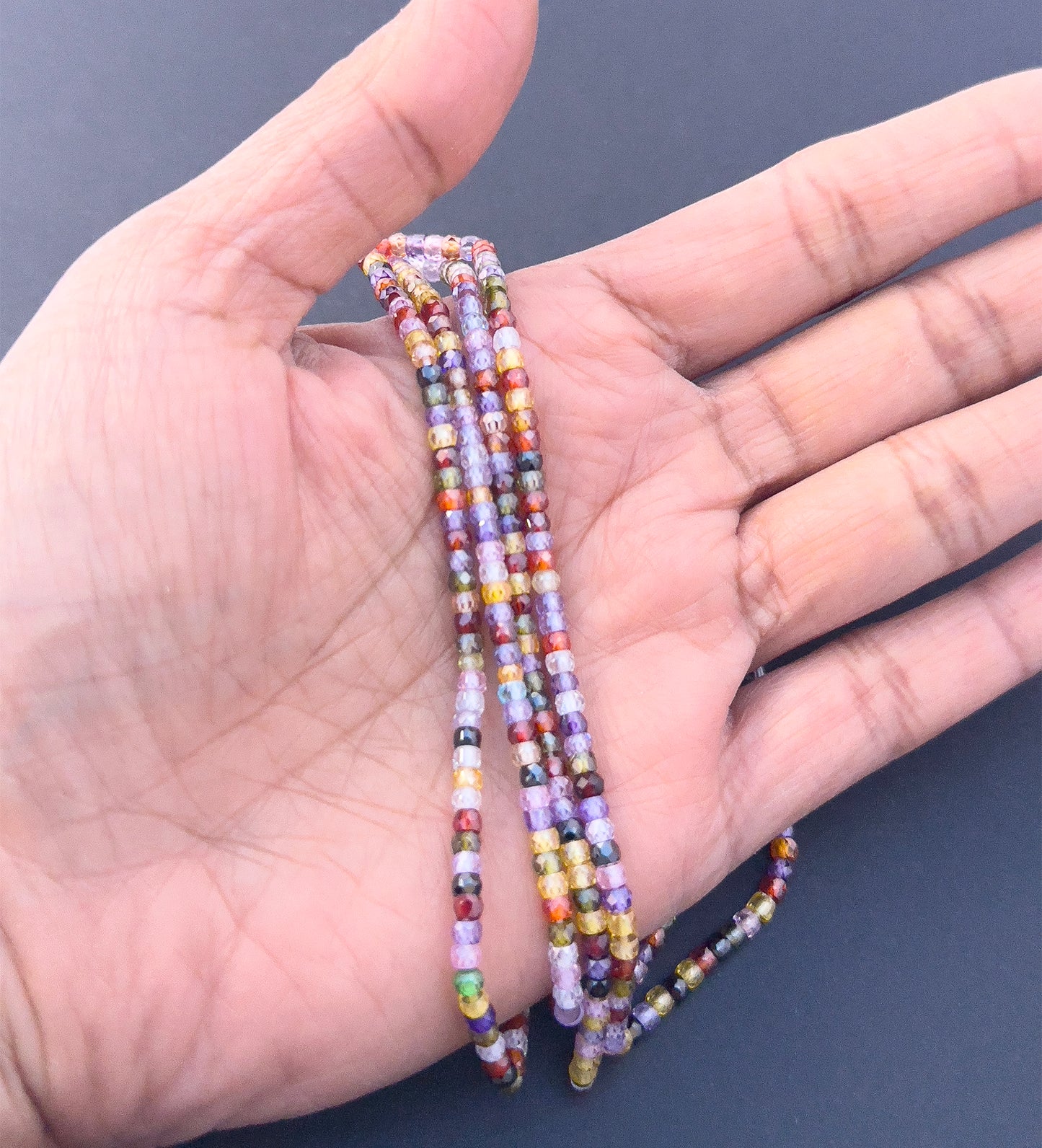 A person holds delicate strands of Cubic Zirconia beads, showcasing their smooth design.