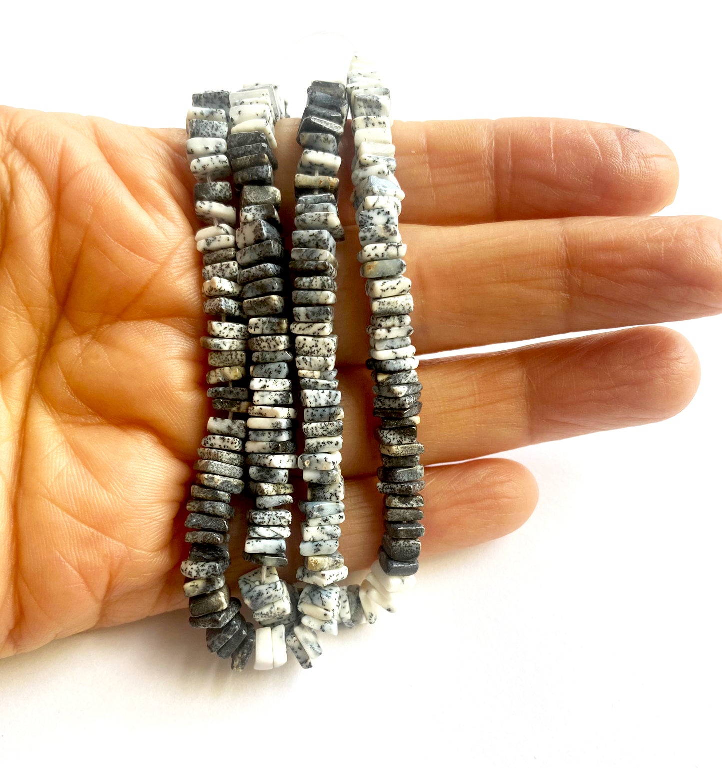 A person holds delicate strands of Dendrite Opal beads, showcasing their smooth design.