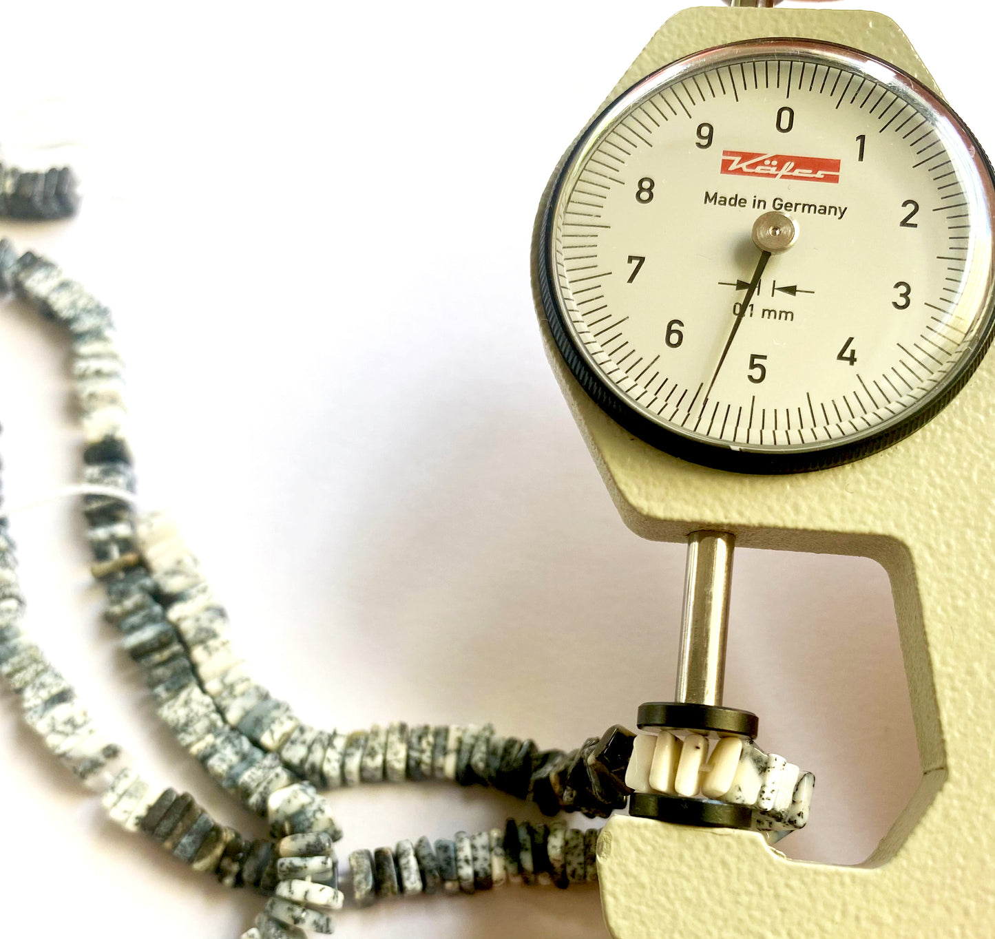 A dial gauge measures the Dendrite Opal Square Heishi 5.3-5.5mm gemstone.