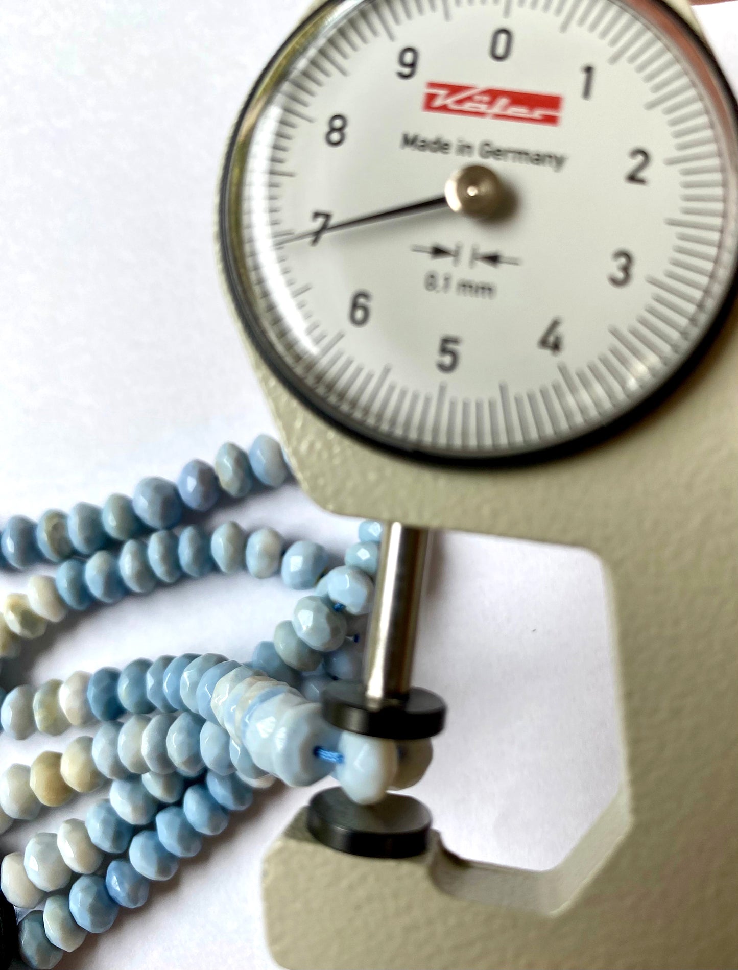 A dial gauge measures the Denim Blue Opal faceted rondelle 6.5mm gemstone, ensuring precision sizing.