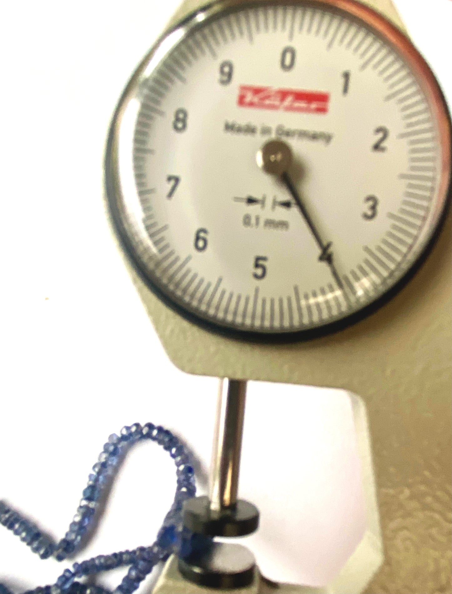 A dial gauge measures the Denim Blue Sapphire faceted rondelle 3–4mm gemstone for precision.