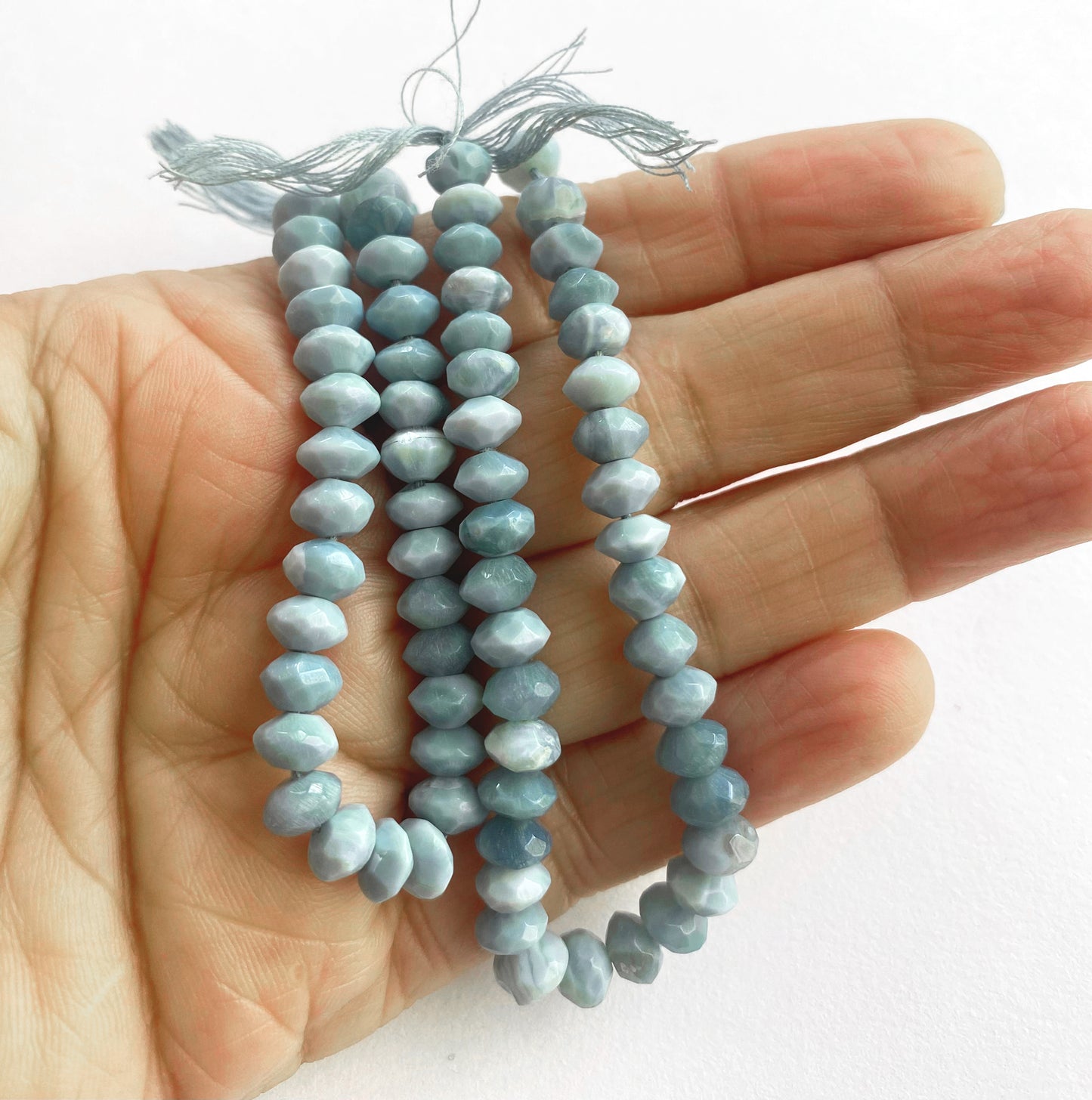 A person holds delicate strands of denim opal beads, showcasing their faceted design.
