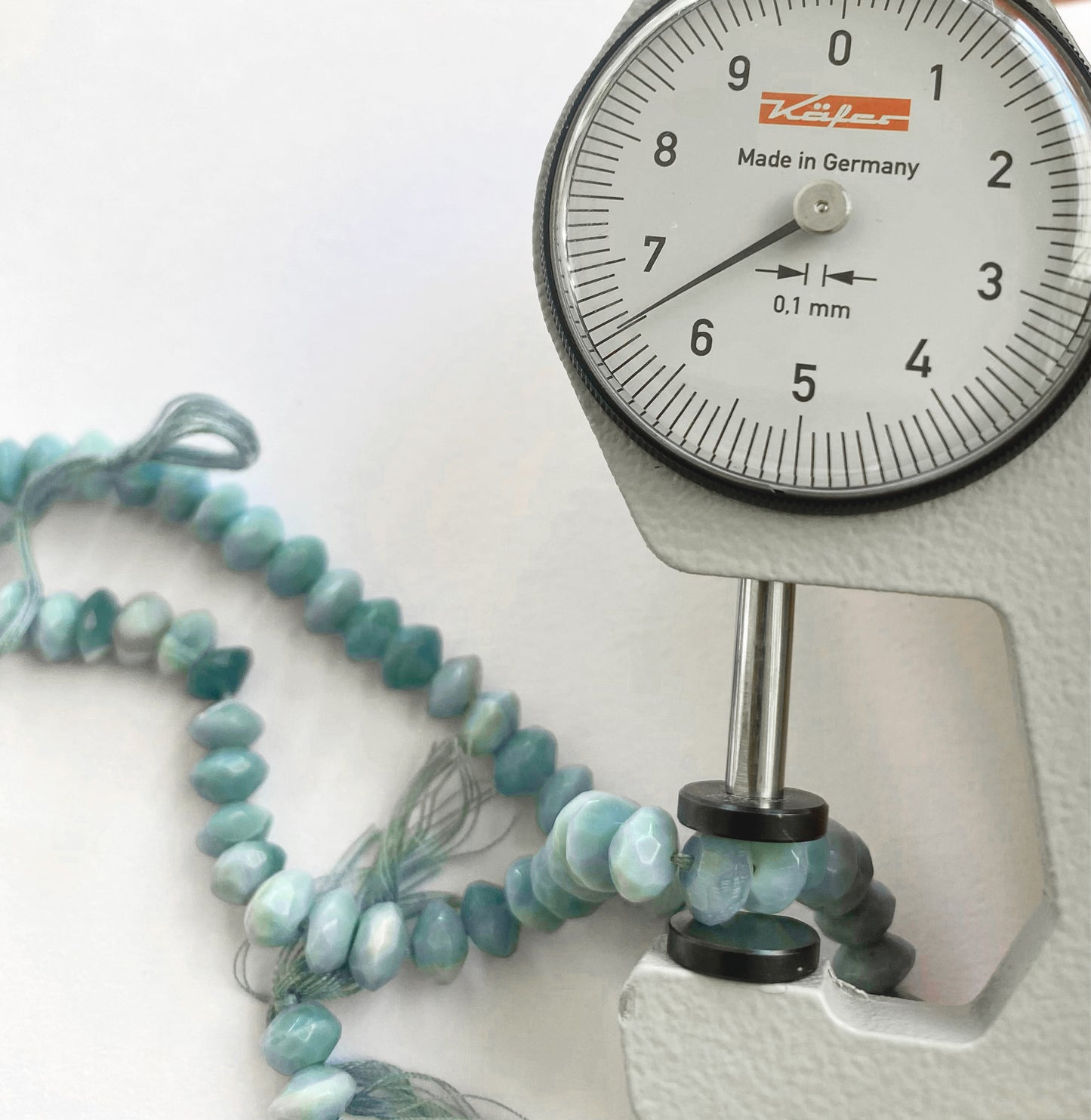 A dial gauge measures the denim opal faceted rondelle 6.5–6.7mm gemstone.