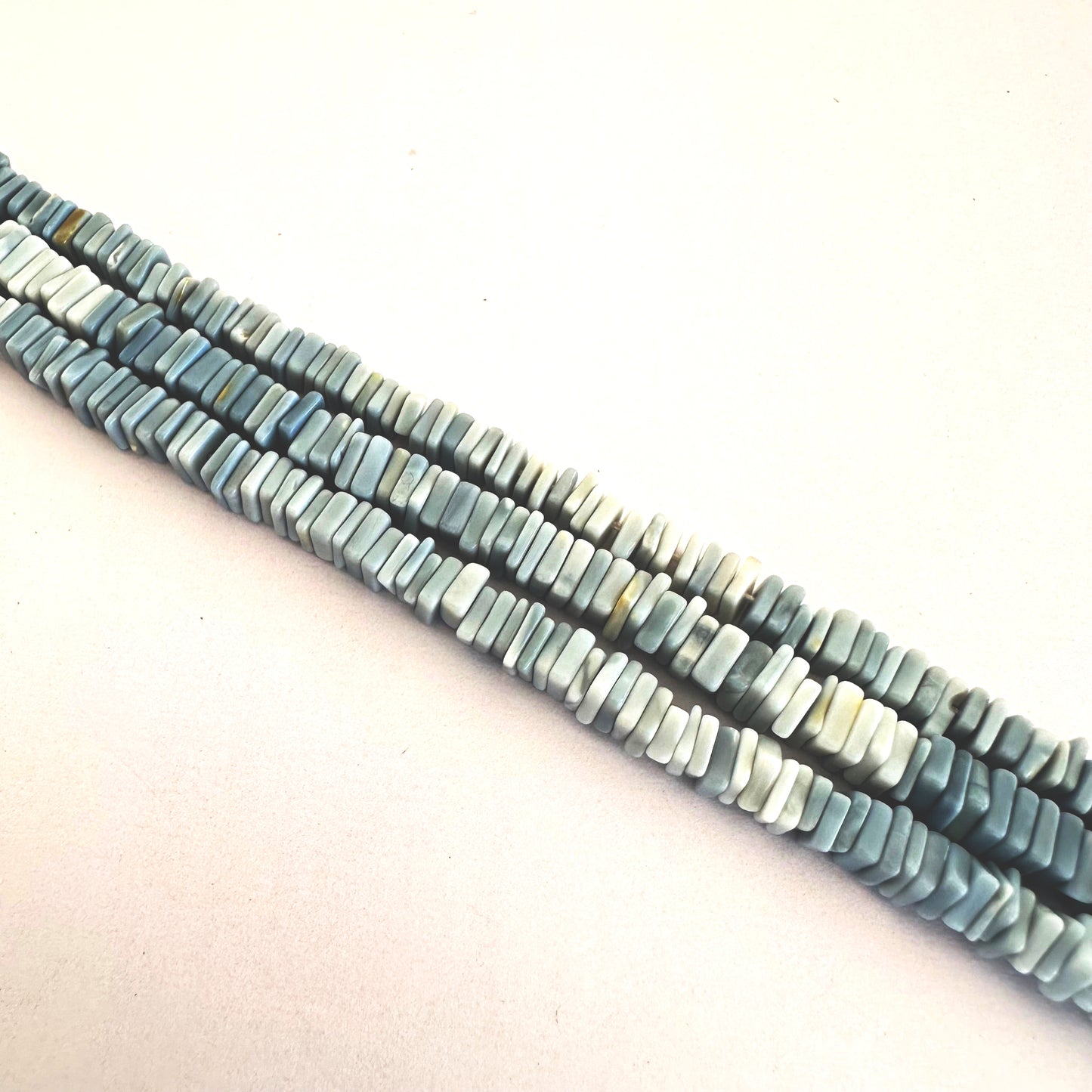 Close-up of 5-5.5mm Denim Opal beads arranged in a clean, linear strand.