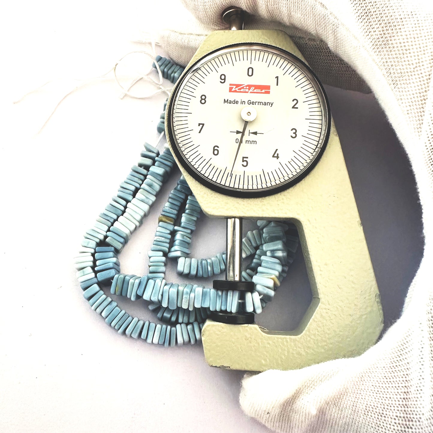 A dial gauge measures the Denim Opal Square Heishi 5-5.5mm gemstone.
