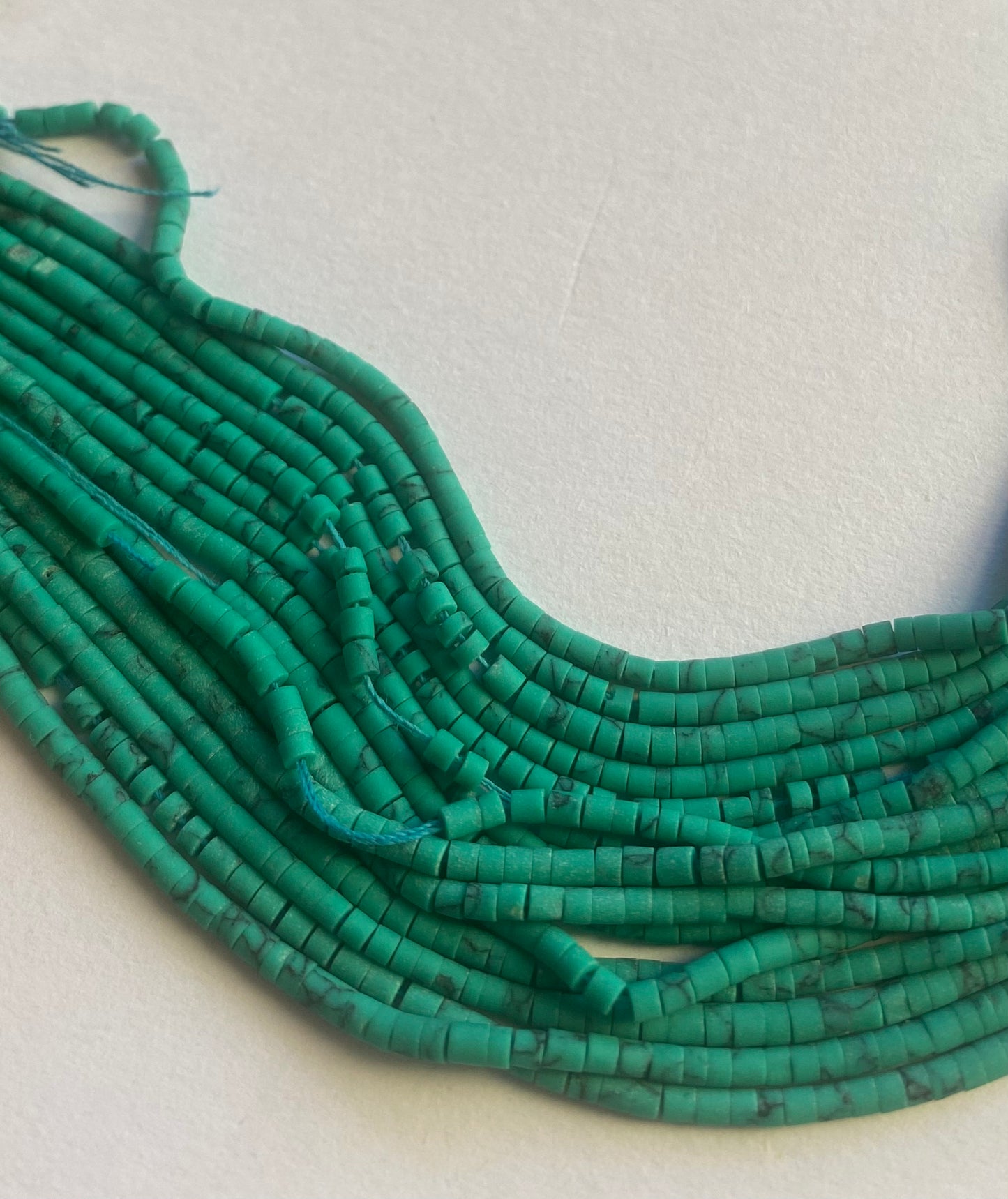 A vibrant assortment of green Afghan tube-shaped heishi beads on a white background, showcasing their unique craftsmanship.