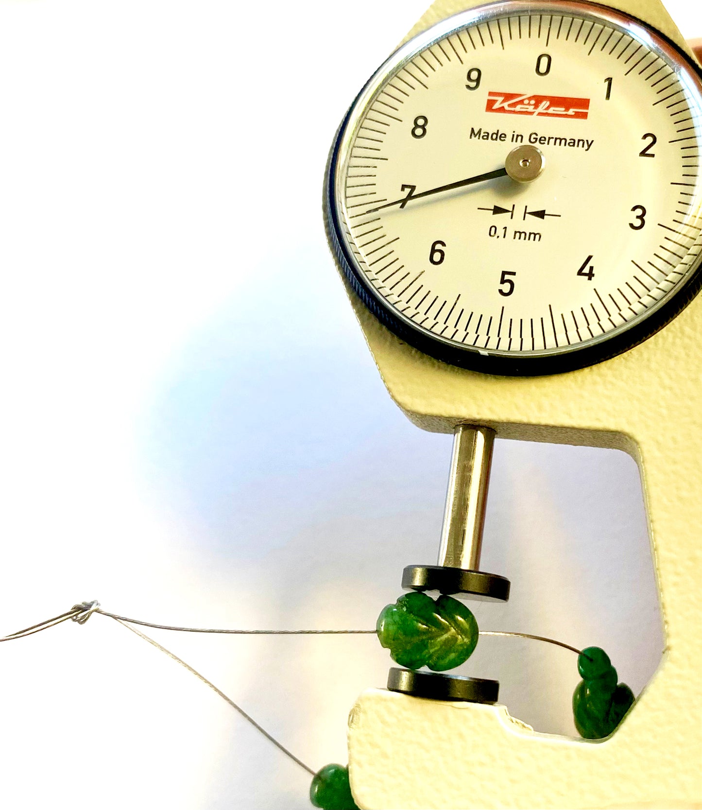 A dial gauge measures the emerald carved gemstone.