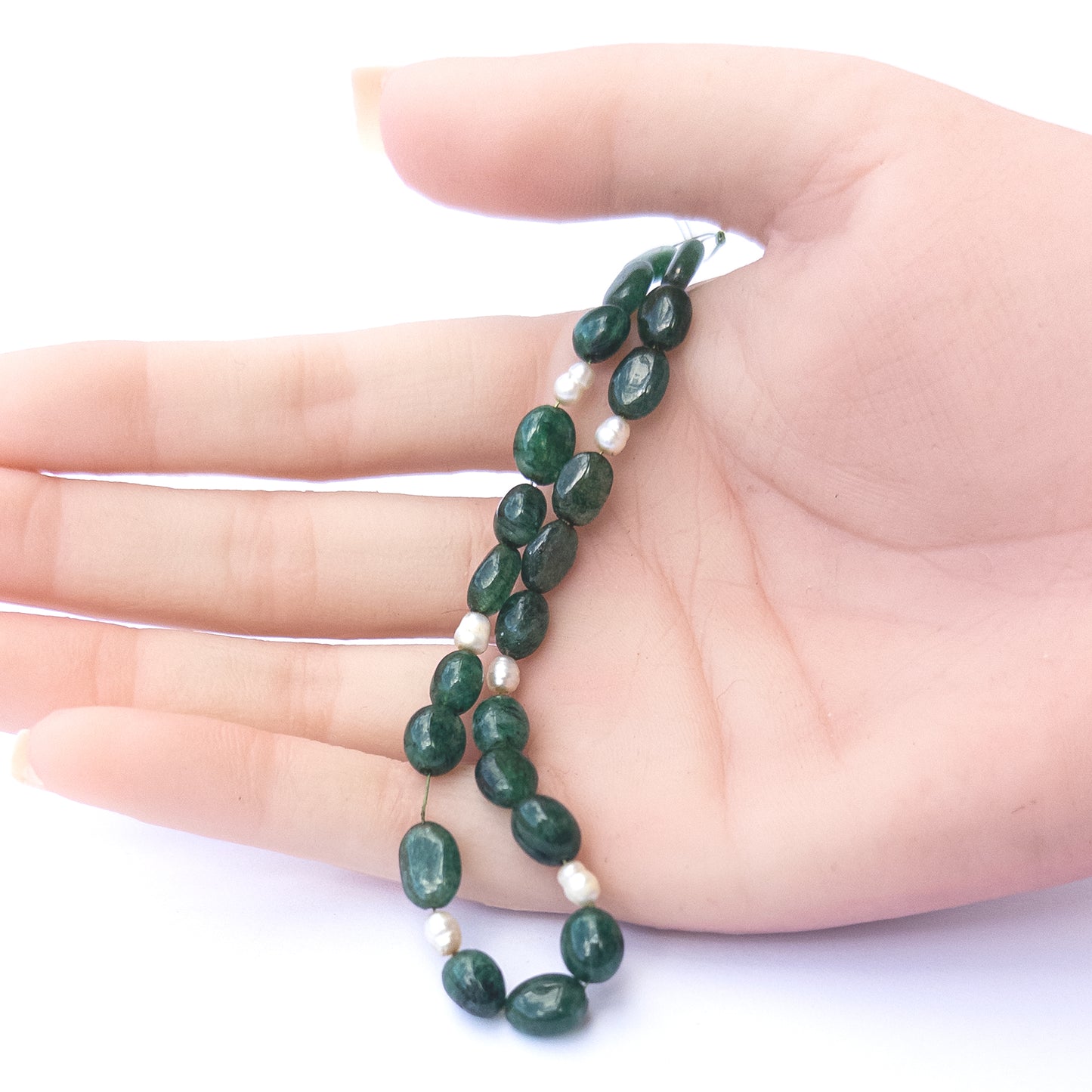 A person holds delicate strands of Emerald and freshwater pearl smooth oval beads, showcasing their polished design.