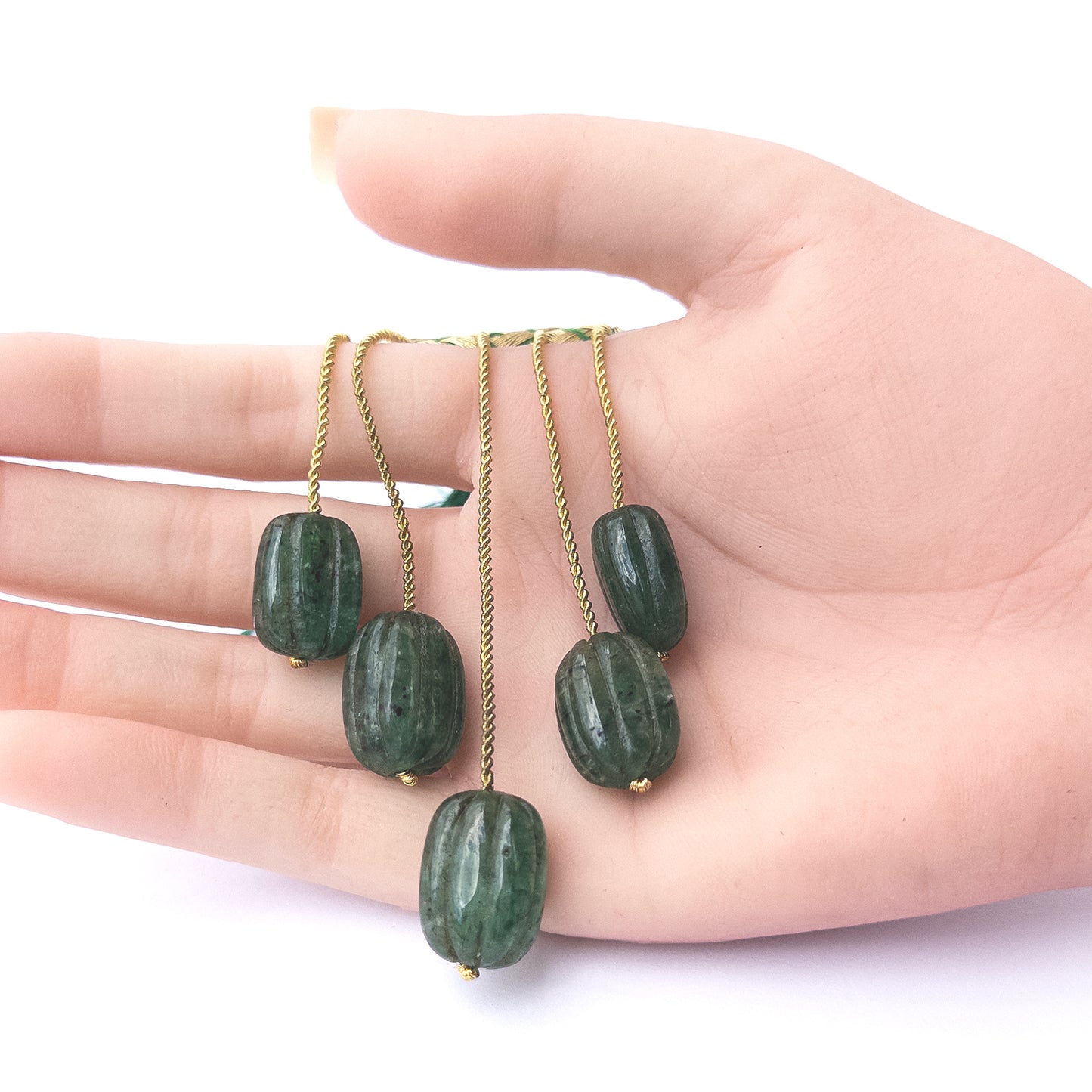 A person holds delicate pieces of Emerald beads, showcasing their carved oval design.