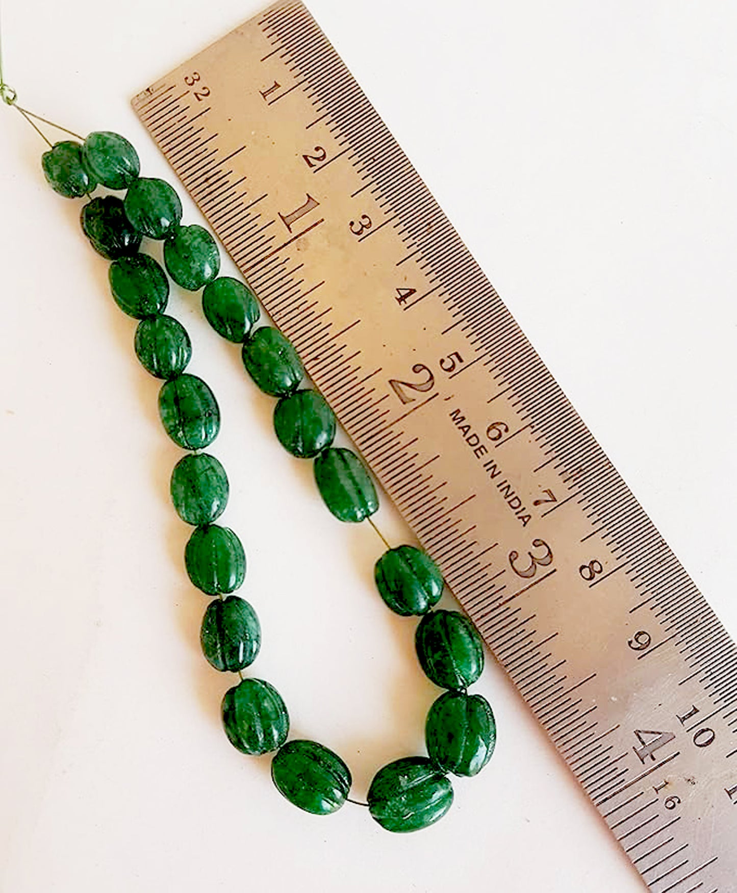A ruler measures the emerald oval gemstone.
